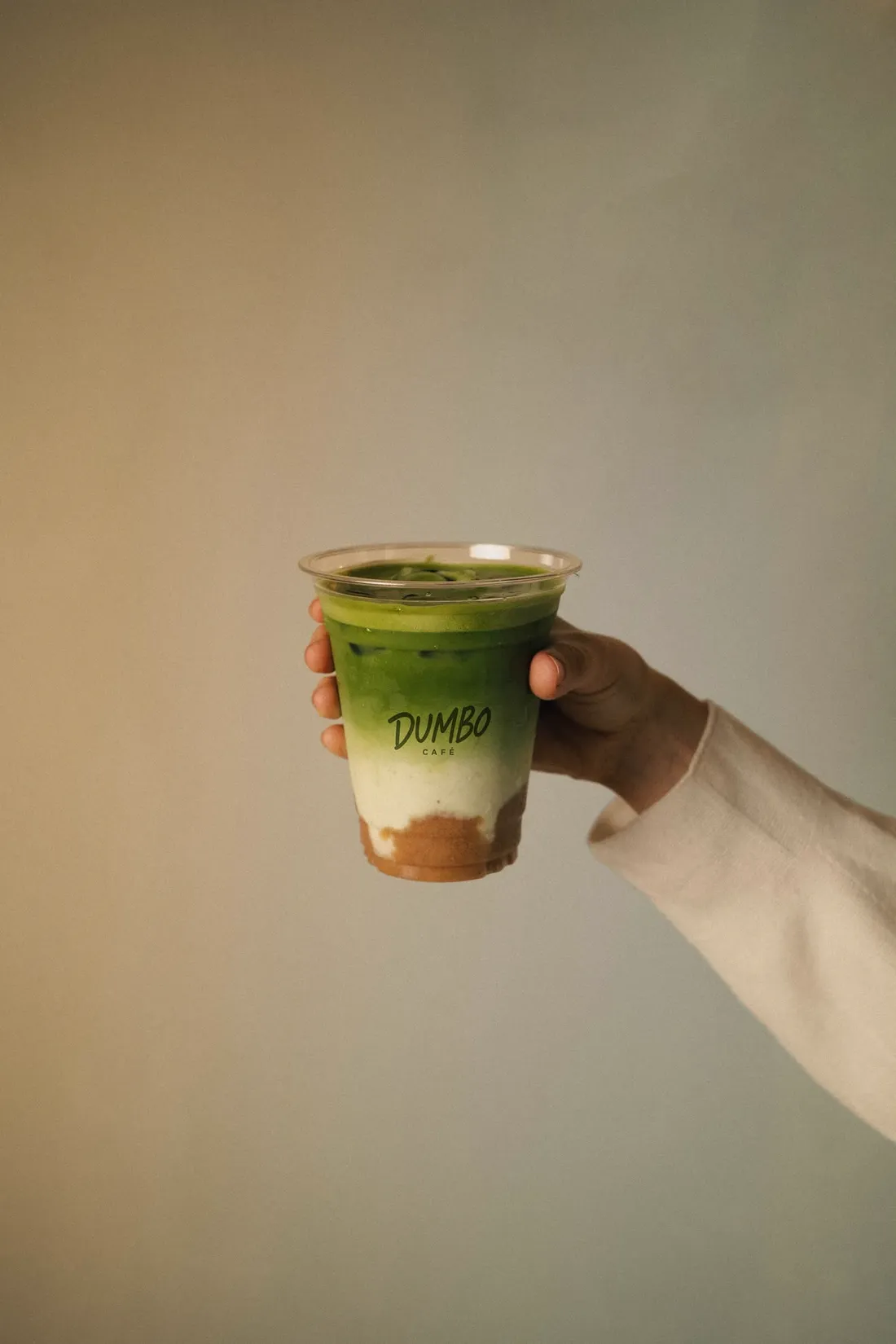 Matcha drink held up against a warm wall